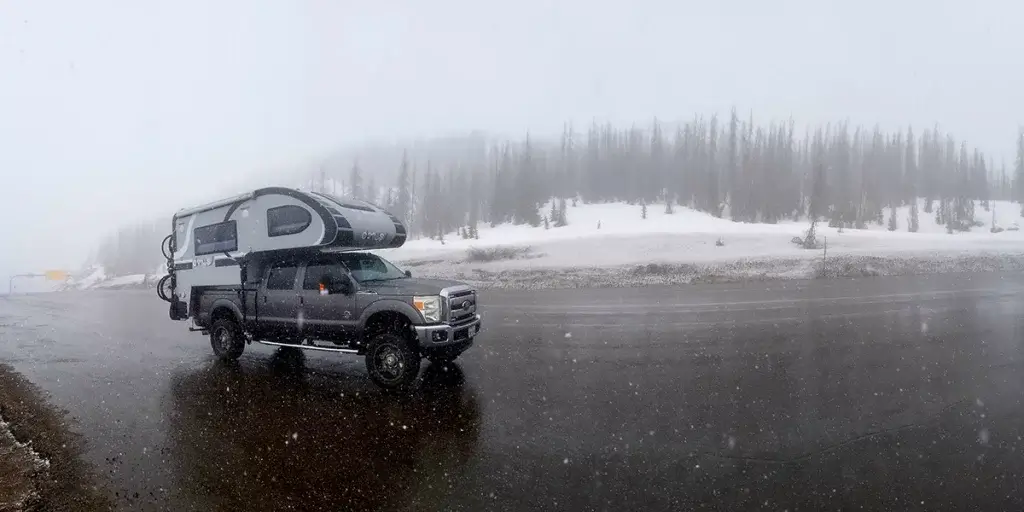 winter camping in a truck camper on road with trees full of snow