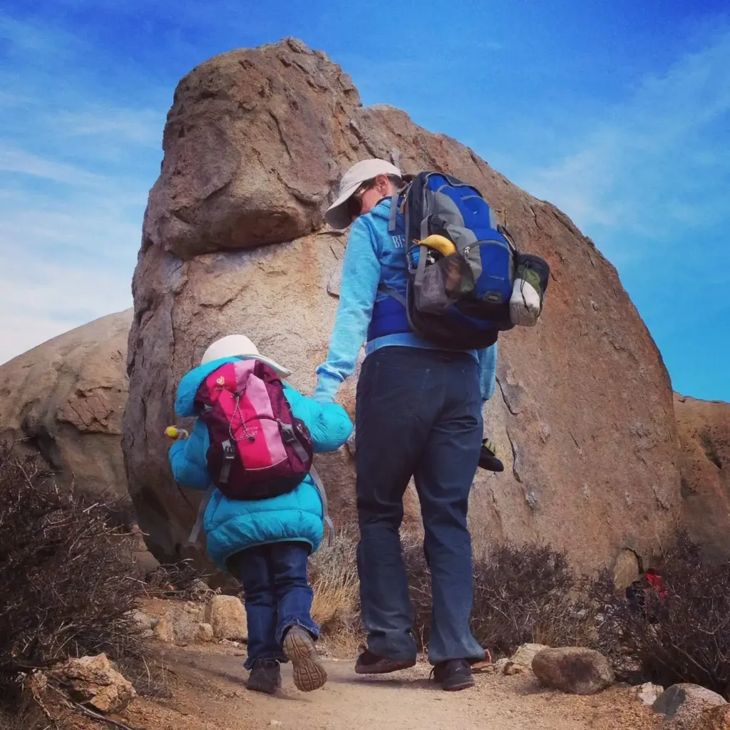 father climbing mountain with kid along with camping bag
