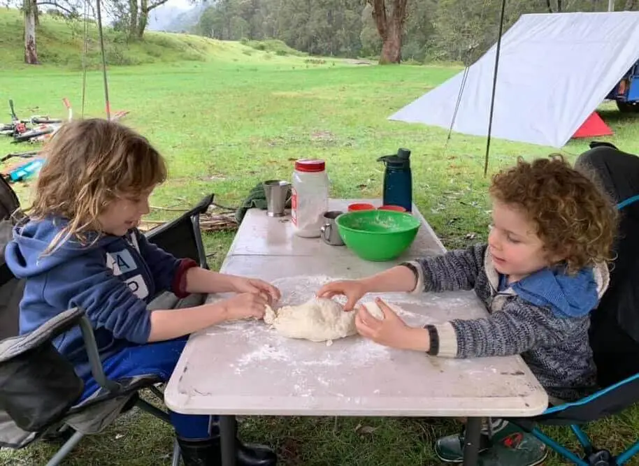 tow kids playing with pizza dough in an outdoor cam sitting on dinning table in green outdoors.