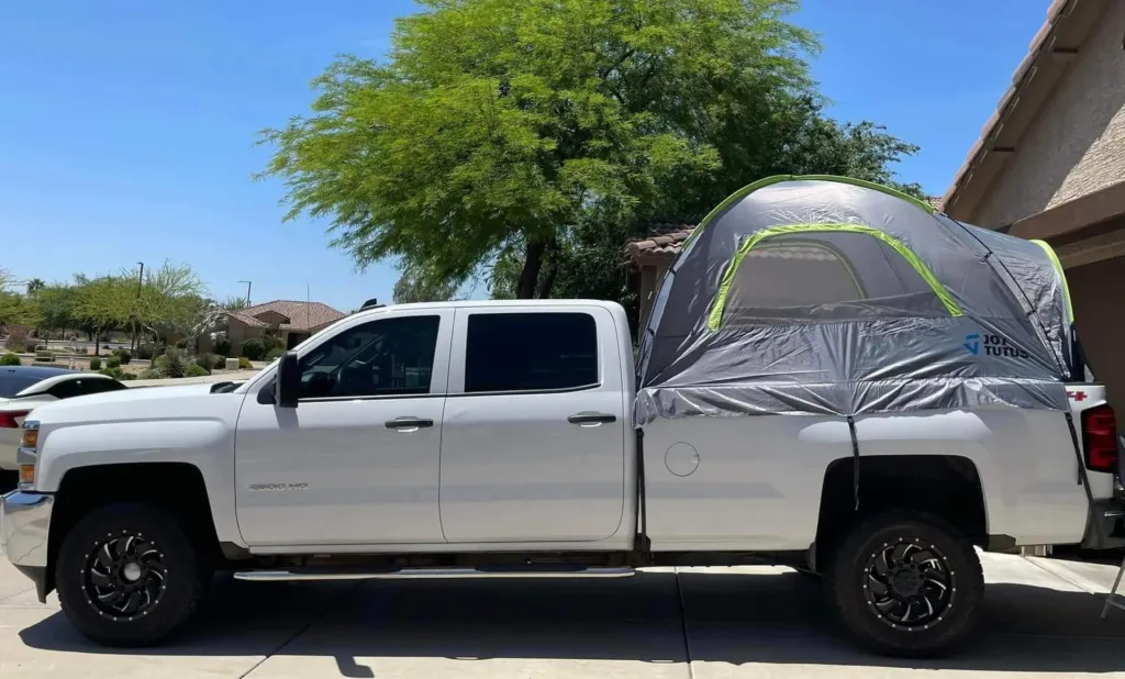truck bed camping while using a truck bed tent on a silver truck parked near road under a tree