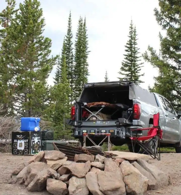 Truck camping using truck canopy with rocks and trees, camping chair, stove, and water tank